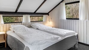 A room with two beds, wooden panel walls, and windows with curtains.