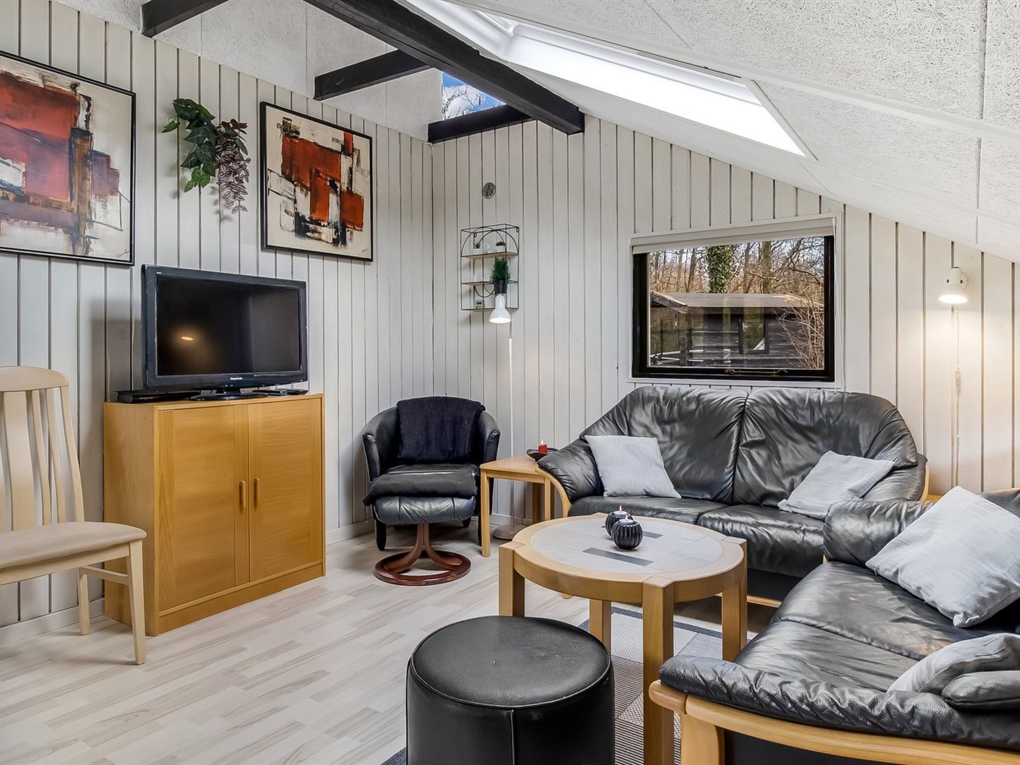 A modern living room with a leather sofa, a television, wooden furniture, and a view through a window.