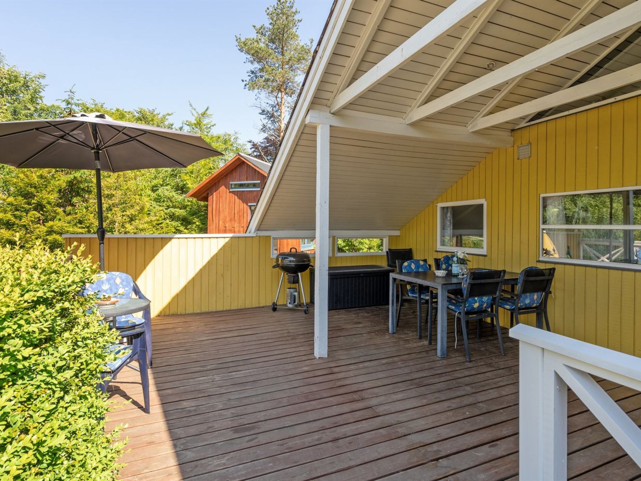 Eine überdachte Terrasse im Freien mit Tisch, Stühlen, einem Grill und einem Sonnenschirm.
