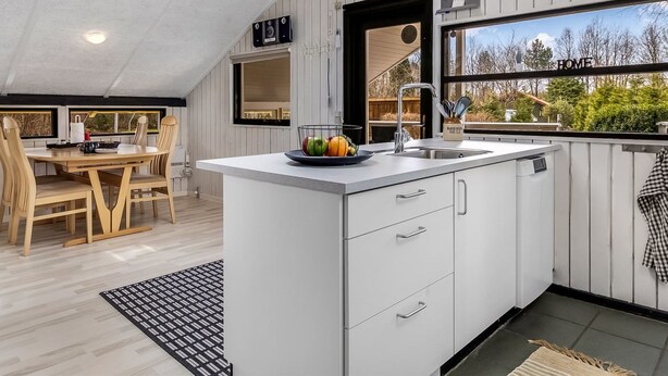A modern kitchen with a central island, white cabinetry, a built-in sink, and a window overlooking greenery.