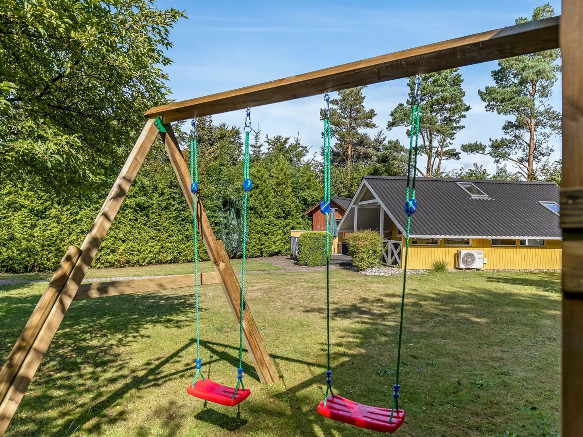 A wooden swing set in a grassy yard with a house in the background.