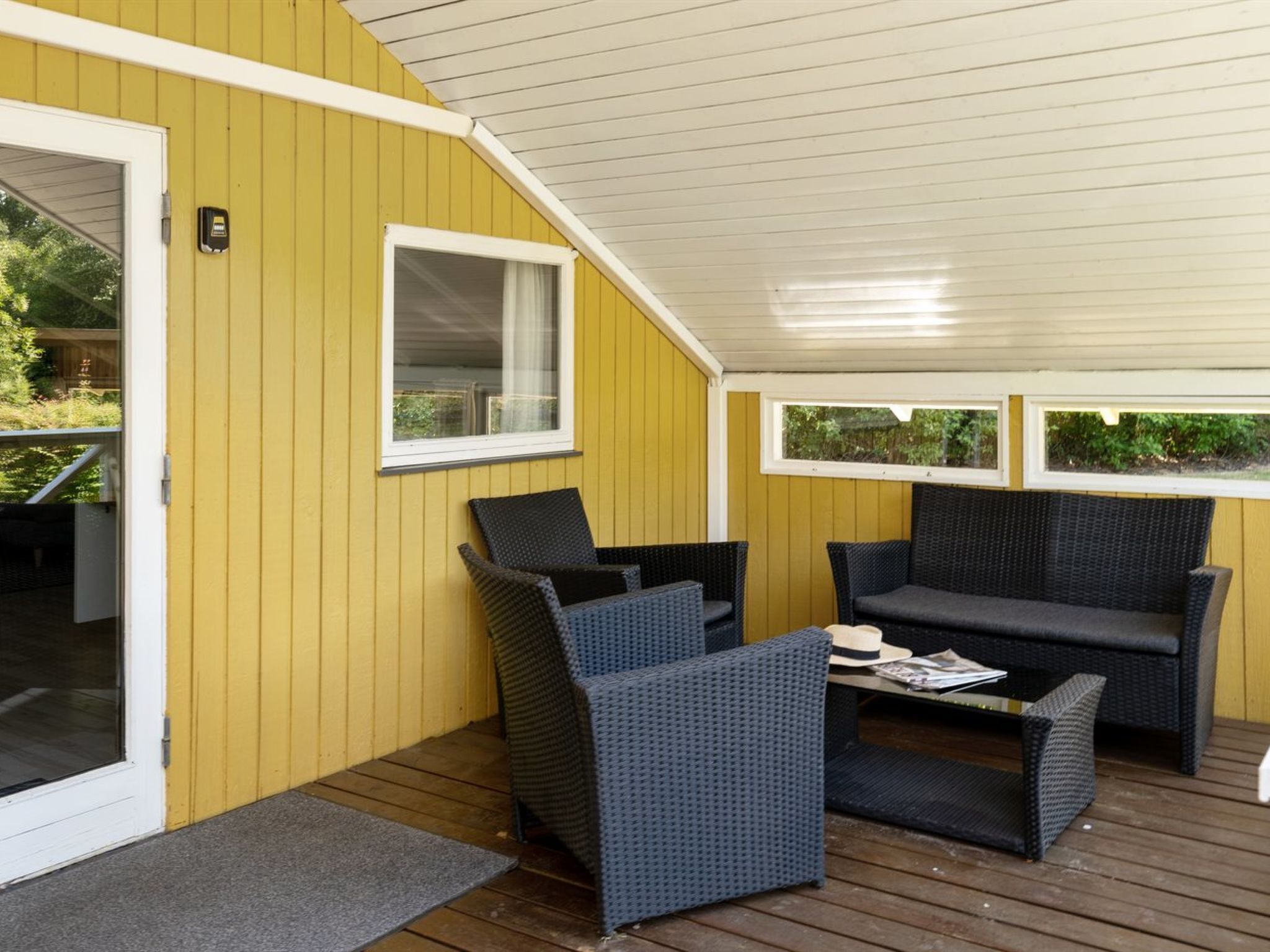 A covered patio area with yellow walls, two wicker sofas, a small table, and a door leading to an outdoor space.