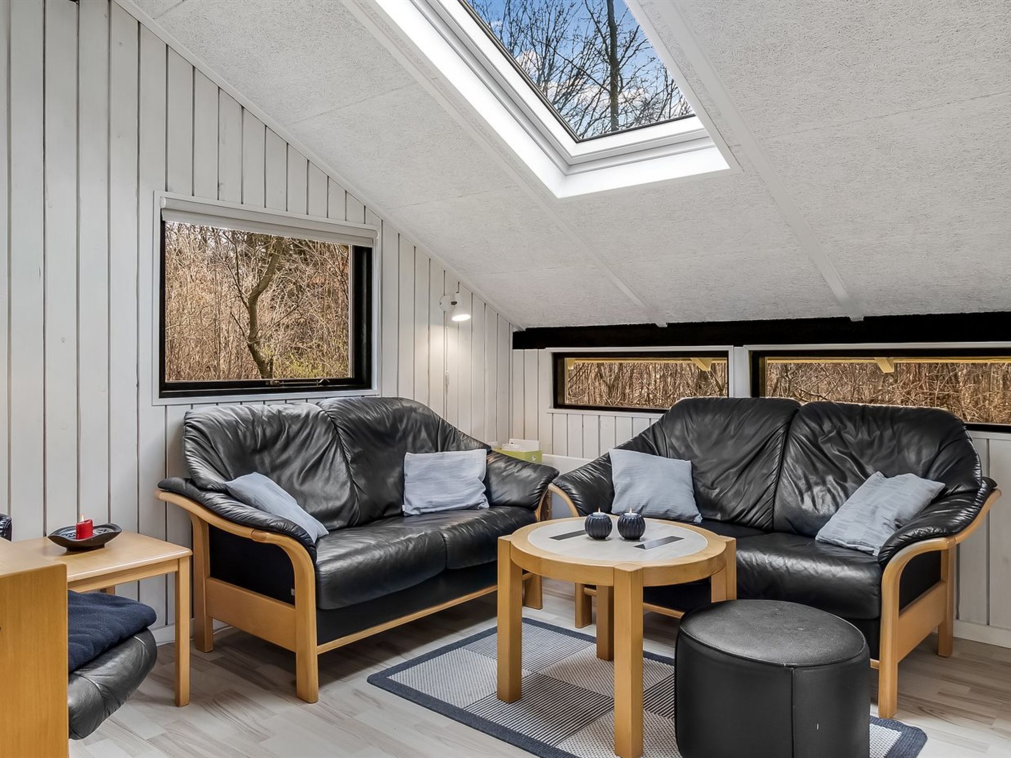 Une chambre à coucher confortable, aménagée en mezzanine, avec un puits de lumière, deux canapés en cuir noir, une table ronde en bois et un petit pouf.