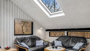 A cozy loft bedroom with a skylight, two black leather sofas, a round wooden table, and a small ottoman.