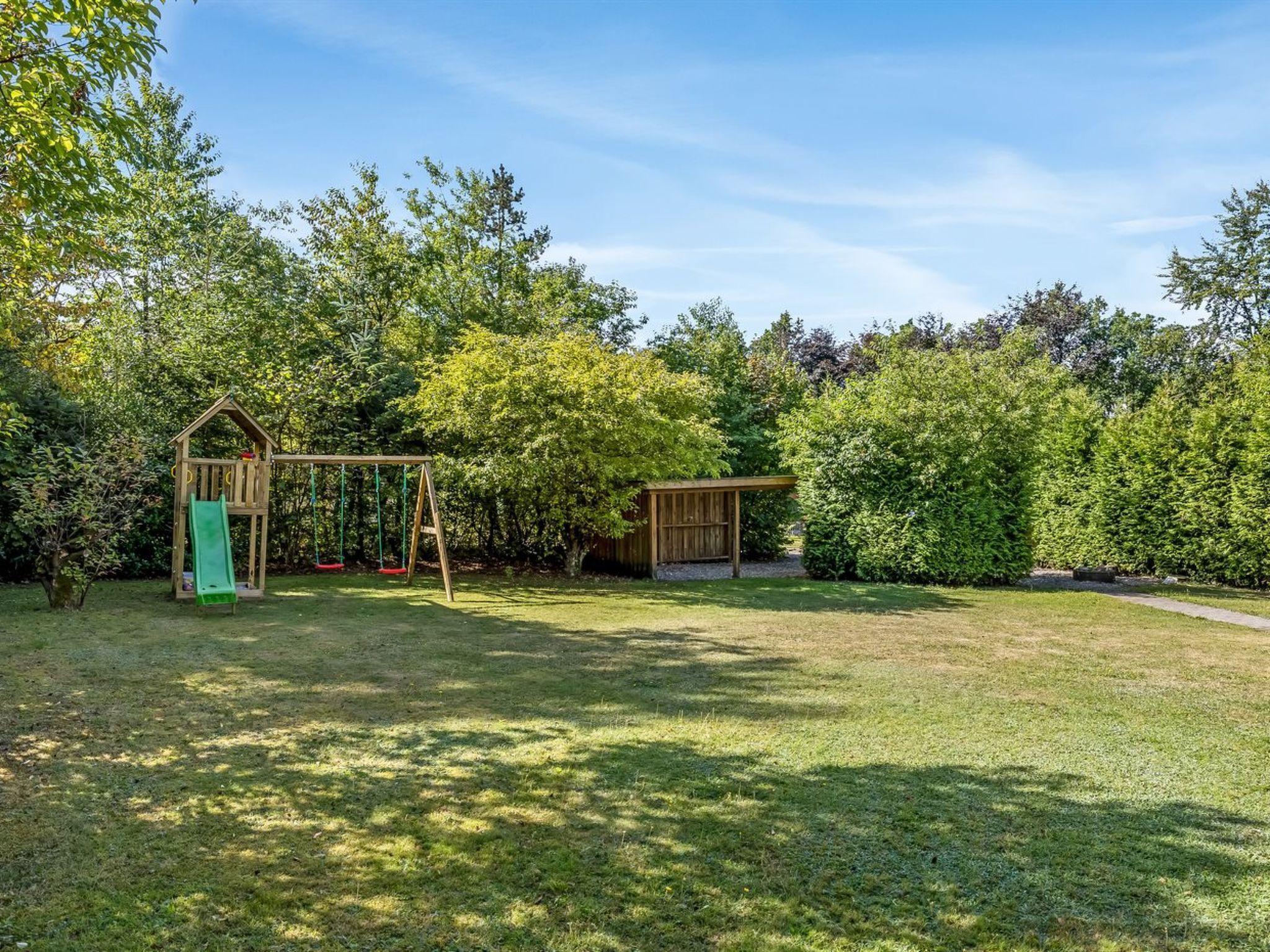 A backyard with a wooden playhouse, a swing set, and a fenced area.
