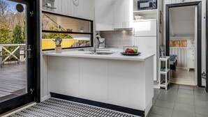 A modern kitchen with white cabinetry, a built-in microwave, and a large window overlooking a deck.