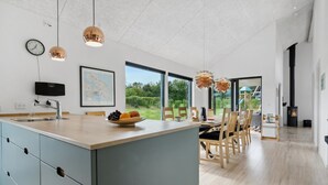 Een moderne keuken met een groot eiland, een eetgedeelte met stoelen, een klok en een zwart fornuis.