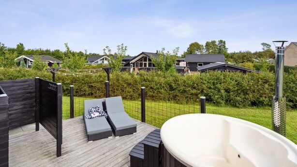 Een terras met twee lounge stoelen, een hottub en een houten omheining.