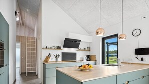 Een moderne keuken met een centraal eiland, houten vloer en uitzicht op het buiten.