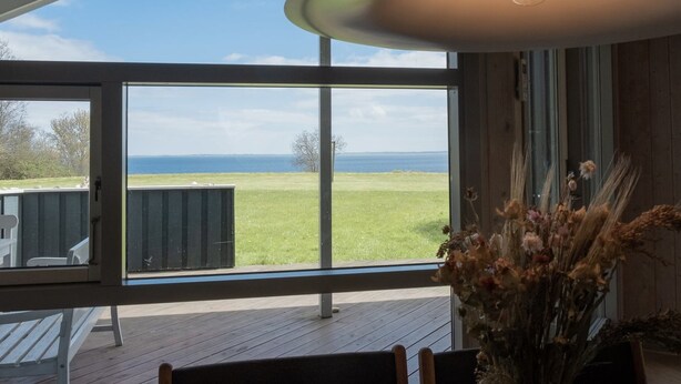 Ein Zimmer mit großem Fenster und Blick auf eine Wiese sowie das Meer.
