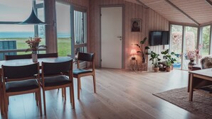 Ein geräumiges Zimmer mit Holzböden, einem Essbereich mit Stühlen, einem Tisch und einem an der Wand befestigten Fernseher.