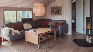 Ein gemütliches Wohnzimmer mit Holzbalkendecke, einem grauen Sofa, einem Holztisch und einem Kamin.