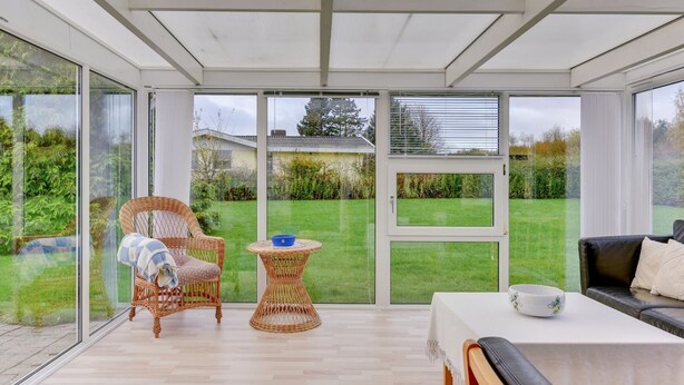 Ein Wintergarten mit Glastür, Korbmöbeln, einem Tisch und Blick auf einen grünen Garten.