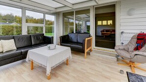 Ein Wintergarten mit einer schwarzen Ledersofa, einem Holzstuhl, einem Tisch mit weißer Tischdecke und Blick ins Freie.