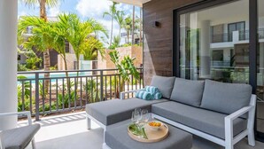 Un balcon avec un canapé gris, une petite table sur laquelle se trouve un saladier rempli de fruits et des verres, et une chaise blanche.