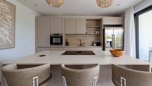 Une cuisine moderne dotée d’un îlot central, de deux luminaires suspendus et d’une grande fenêtre.