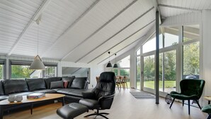 A spacious living room with a large black leather sofa, a black leather chair, and a wooden coffee table. There are two pendant lights hanging from the ceiling, and a large window providing a view of the outdoors. - "Gram" - 450m from the sea by Interhome (Sydals)