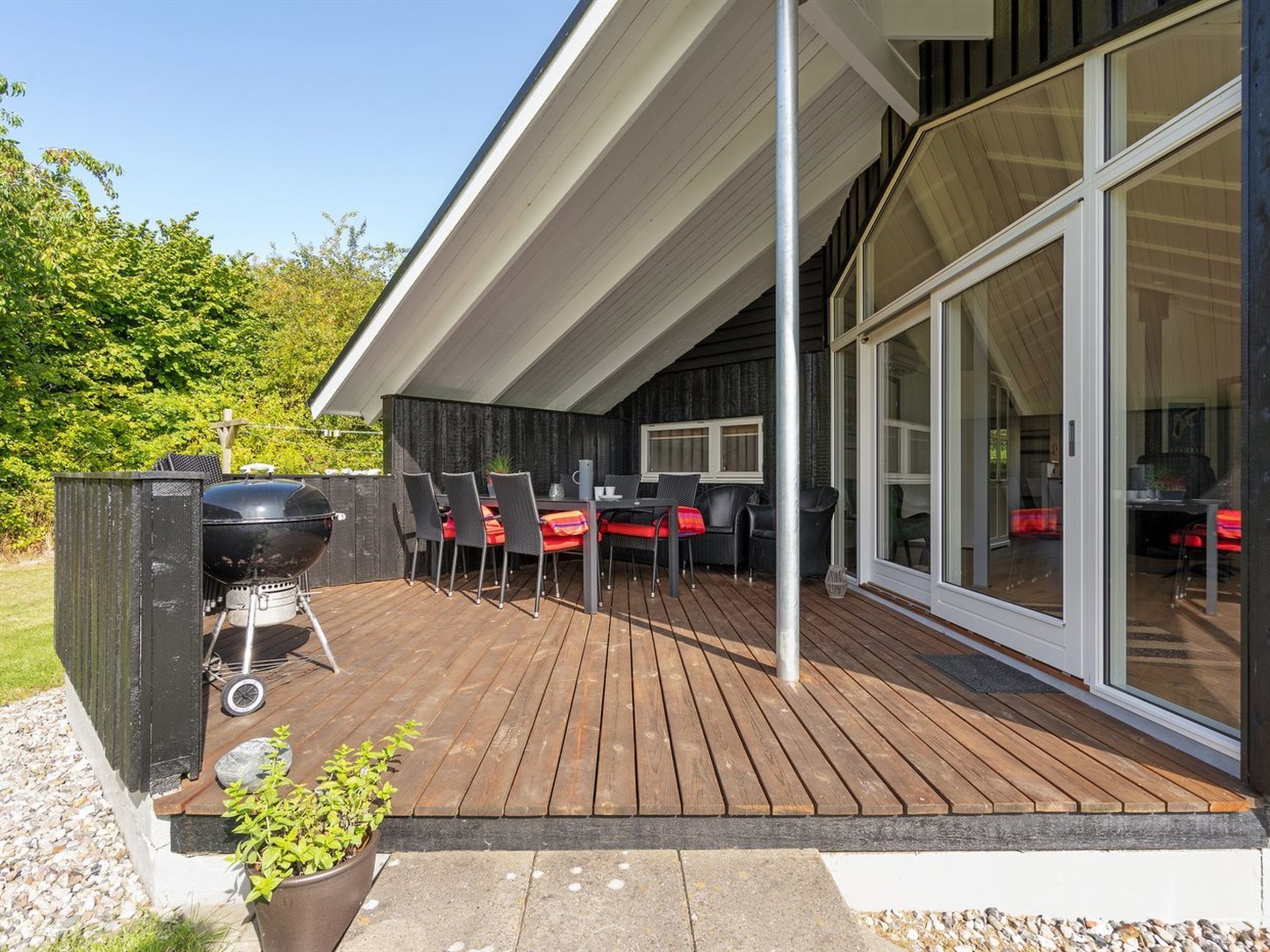 A covered outdoor patio with a grill, seating area, and glass doors leading to an interior space.