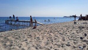 Una playa arenosa con un muelle y gente realizando diversas actividades.