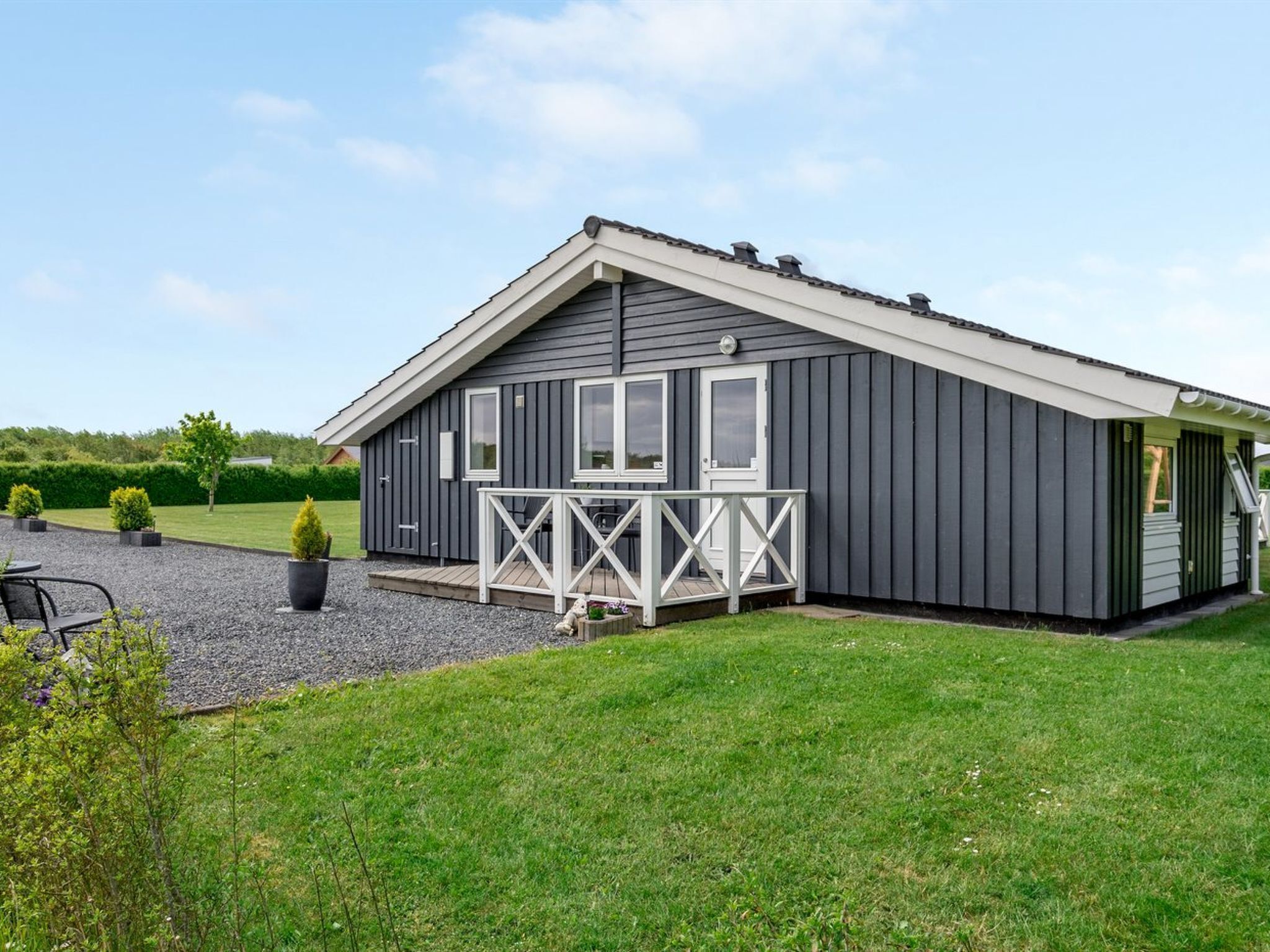 A modern, single-story building with a grey exterior, a white porch, and a small deck area.