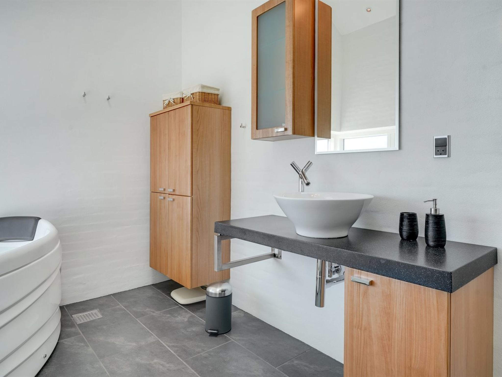 Un baño moderno con un mueble de madera, un lavabo blanco y un espejo encima.