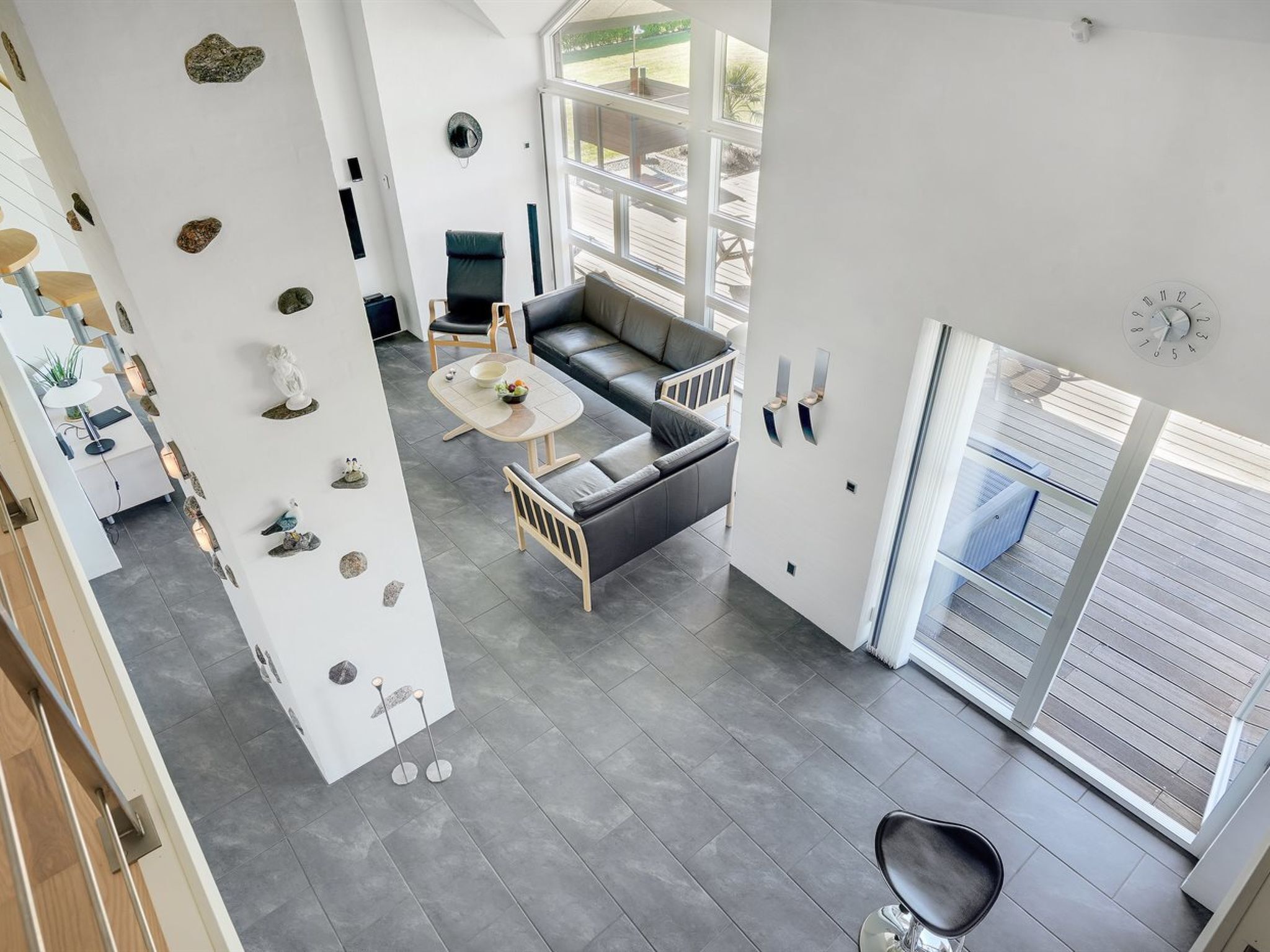 Un salon moderne avec un canapé gris, une table basse et un coin repas comprenant une table et des chaises blanches. On y trouve également des pierres décoratives et une horloge murale.
