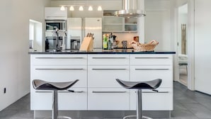 Een moderne keuken met een centraal eiland, roestvrijstalen apparatuur en barstoelen.