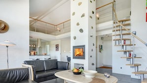 Een moderne woonkamer met een zwarte leren bank, een ronde salontafel met fruit en een open haard.