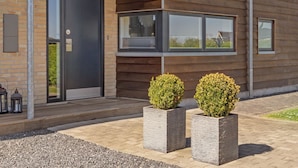 Een modern gebouw met een bakstenen gevel, grote ramen en twee vierkante plantenbakken met struiken.