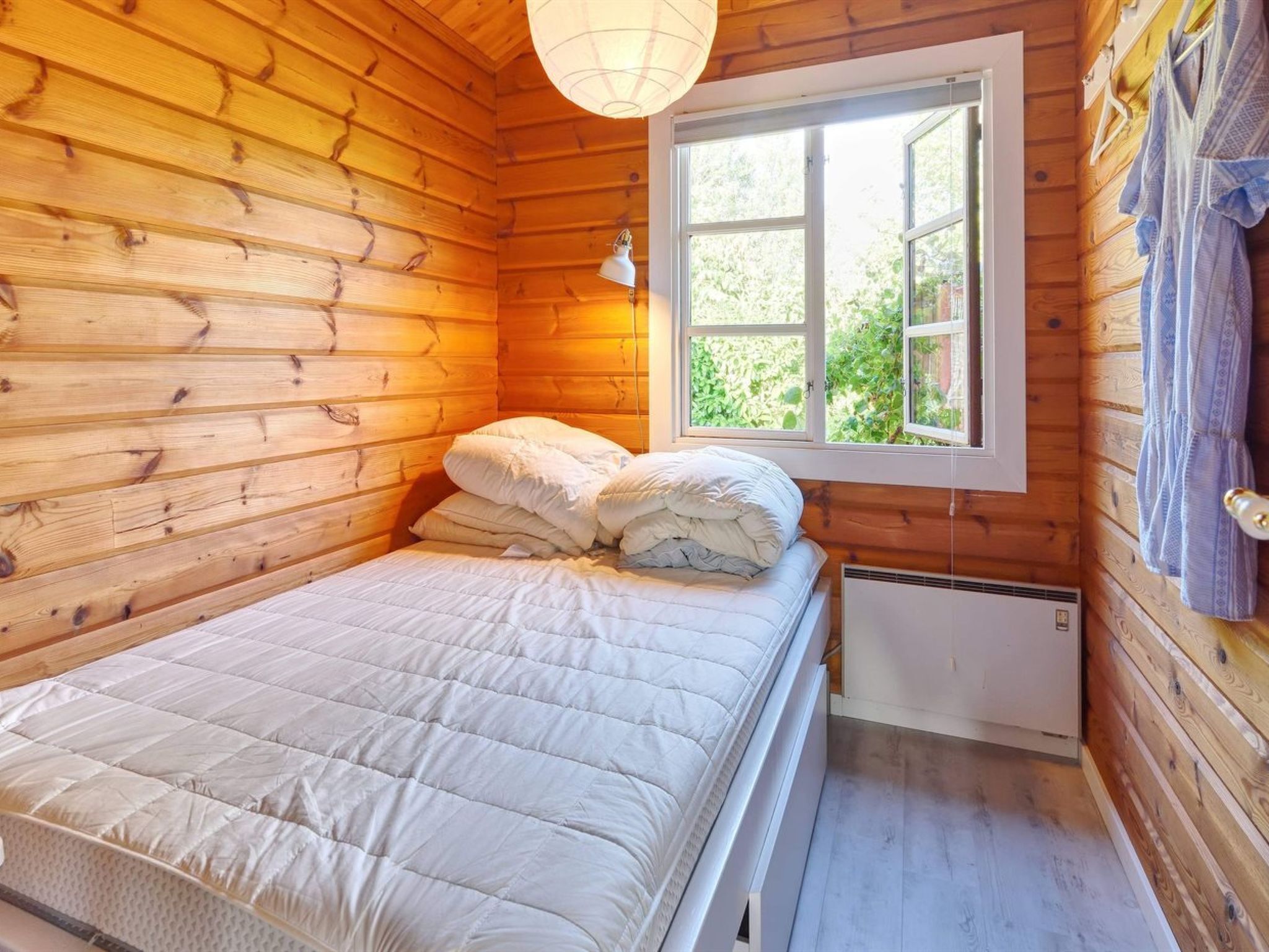 A wooden cabin room with a bed, a window, and a hanging light fixture.