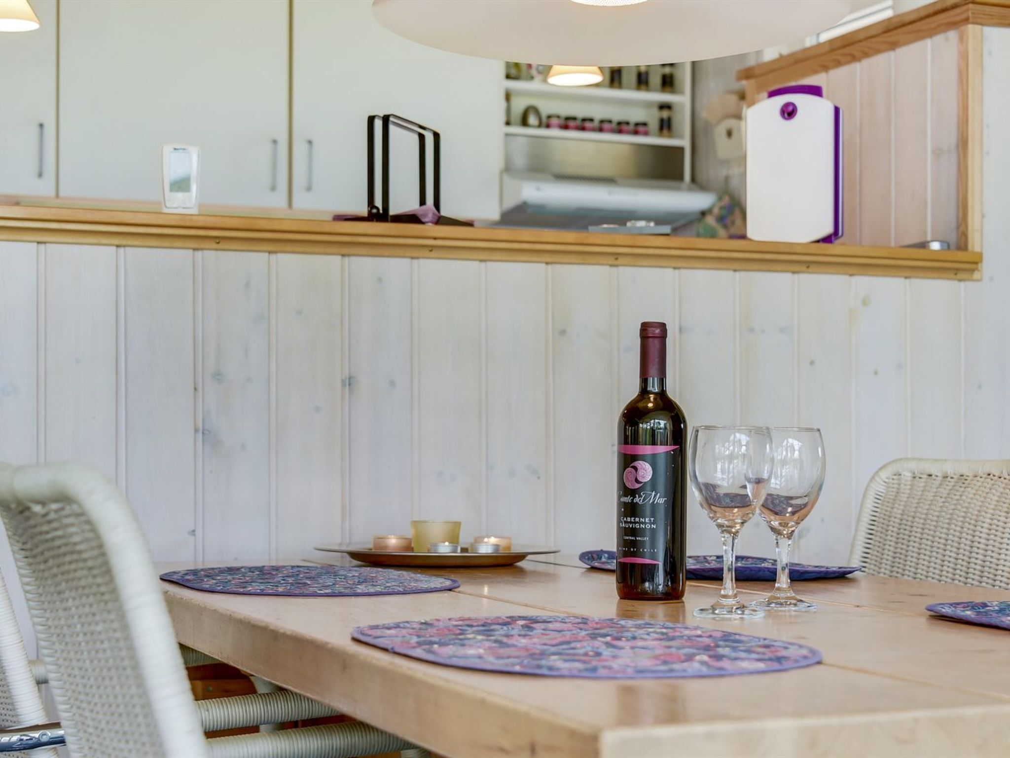 A wooden dining table with placemats, a bottle of wine, and two wine glasses.