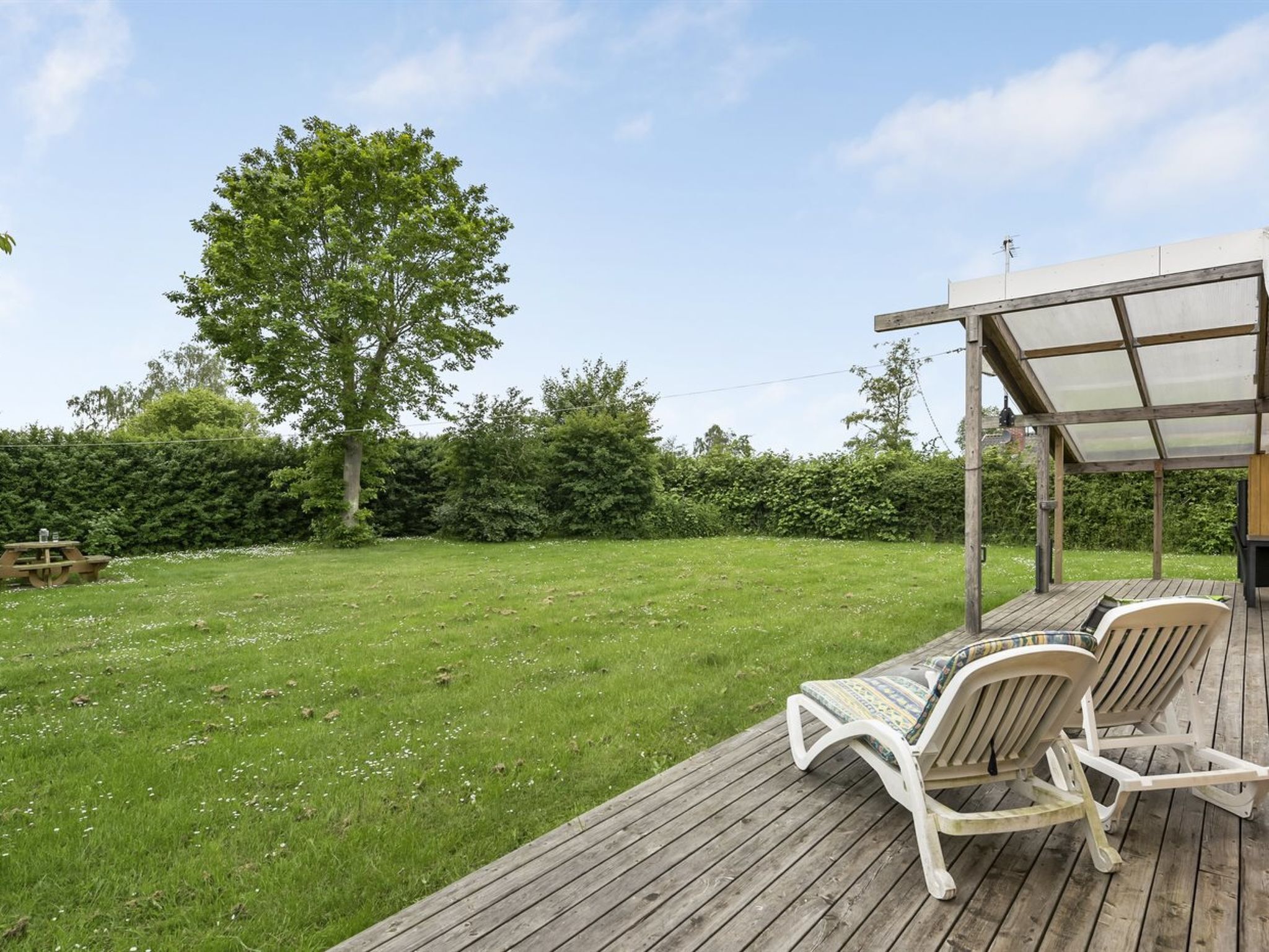 A wooden deck with two white lounge chairs and a covered patio area.