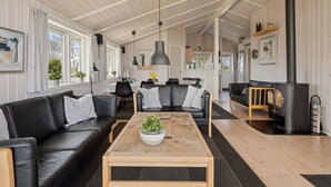A spacious living area with a black leather sofa, a wooden coffee table with a plant, and a large black heater. - "Tjakko" - 900m from the sea by Interhome (Sydals)