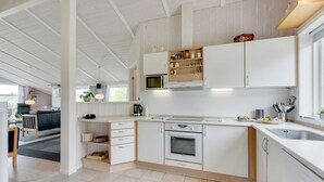 A modern kitchen with white cabinetry, a microwave, and a sink. There is a dining area with a table and chairs visible in the background. - "Tjakko" - 900m from the sea by Interhome (Sydals)