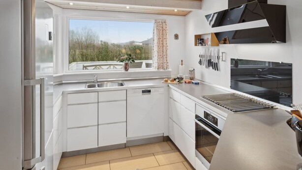 Una cocina moderna con armarios blancos, horno empotrado y un amplio ventanal con vistas al exterior.