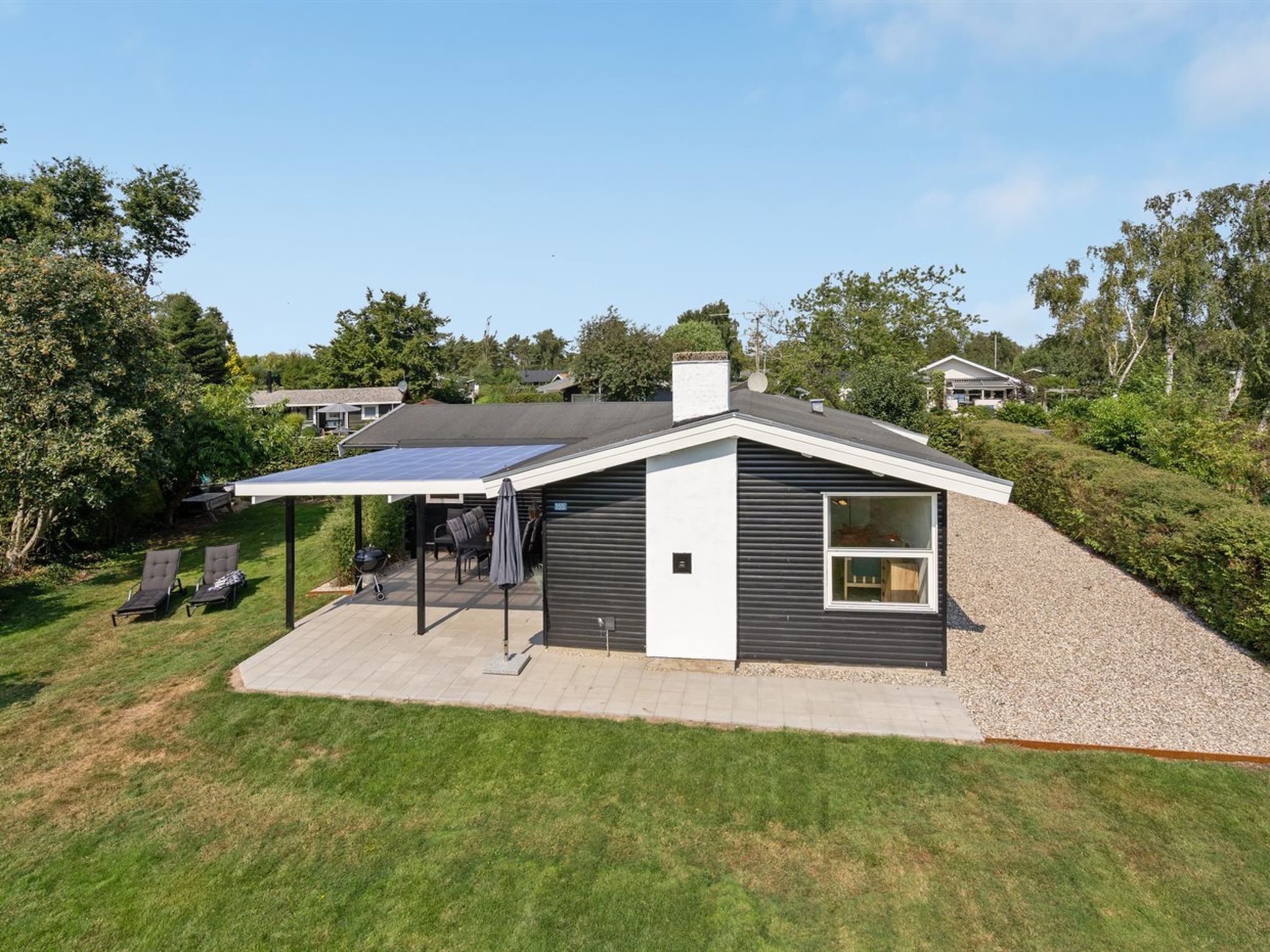 A modern house with a covered patio, a solar panel, and a well-maintained lawn.