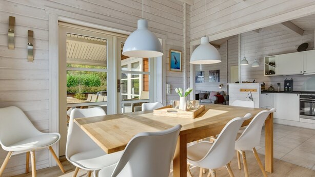 A modern kitchen with white cabinetry, a wooden dining table, and pendant lights.