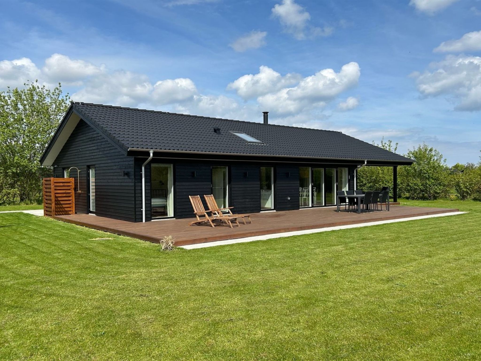 A modern black house with a covered patio, two lounge chairs, and a dining table.