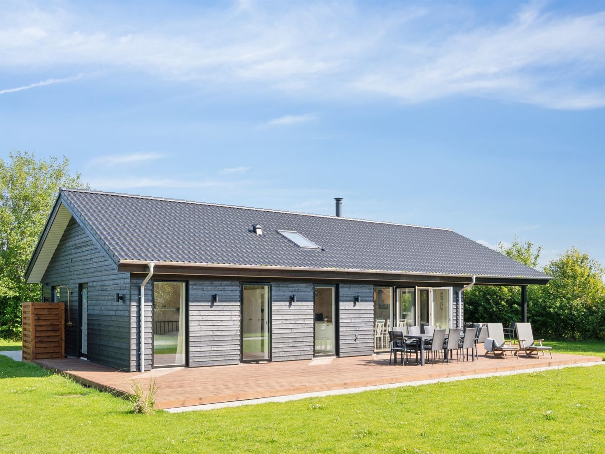 A modern house with a sloped roof, large glass doors, and a patio with outdoor furniture.