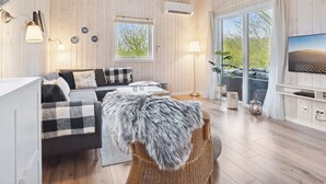 A cozy living room with a sofa, a television, and a large window offering a view of greenery.