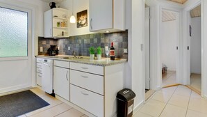 A modern kitchen with white cabinets, a granite countertop, and a backsplash of dark tiles. There is a wine bottle and glass on the counter, and a trash can is visible. - "Umen" - 300m from the sea by Interhome (Sydals)