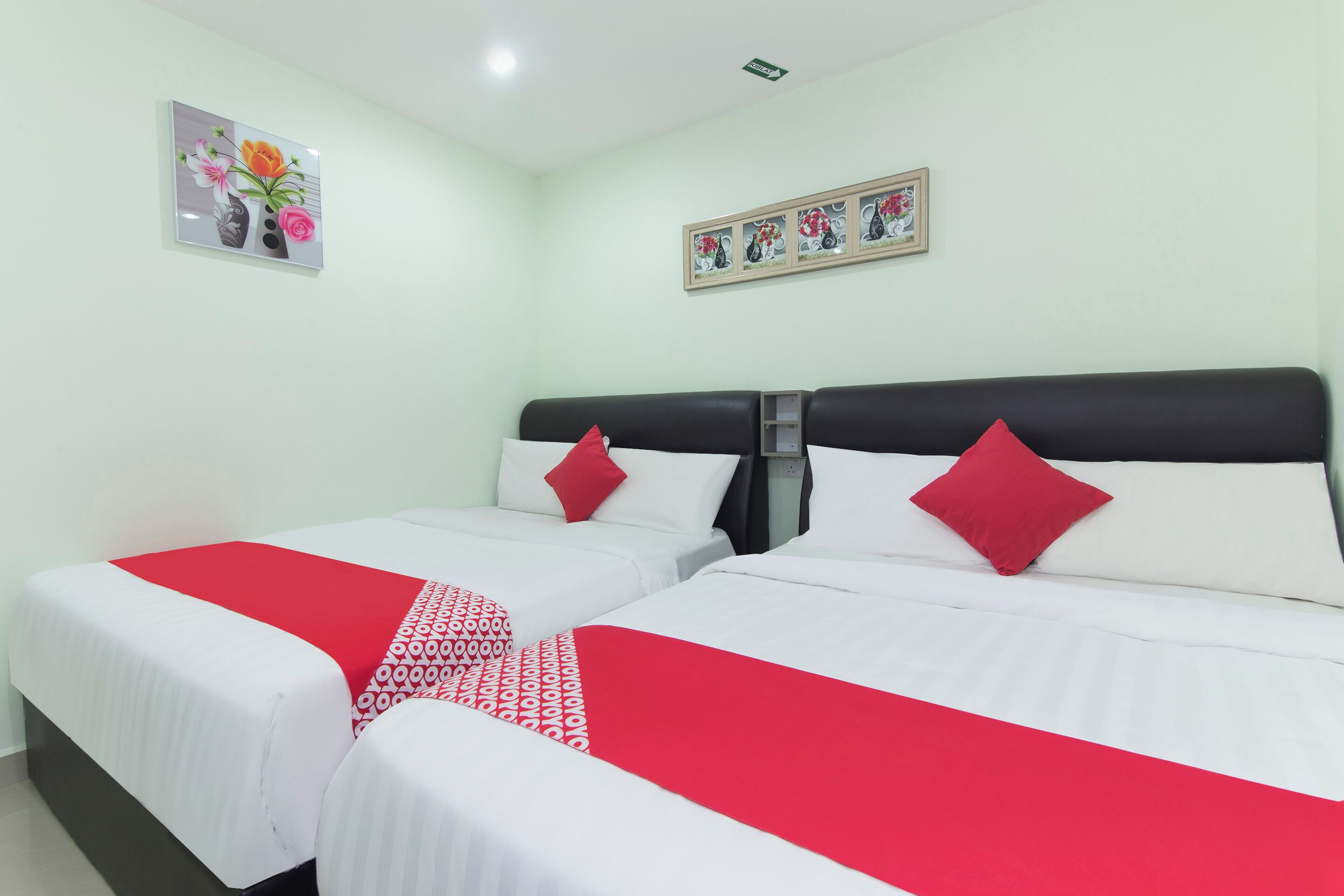 A hotel room with two beds, each with white bedding and red accents, a framed floral artwork above the beds, and a small framed picture on the wall.