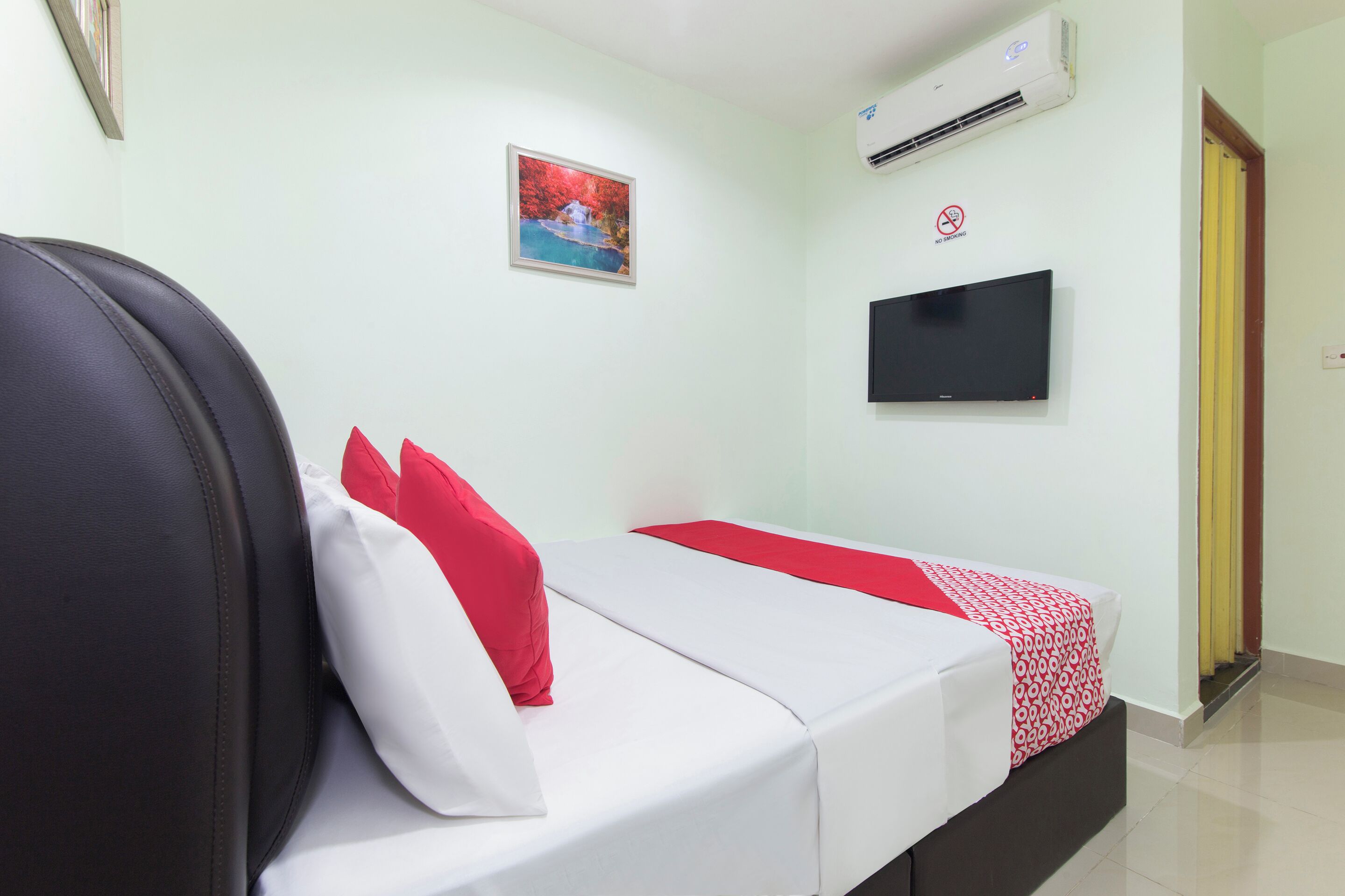 Una habitación de hotel con una cama, un televisor instalado en la pared y un equipo de aire acondicionado.