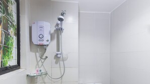 Un baño pequeño con paredes blancas, un inodoro, cabina de ducha y ventana con vistas a la vegetación.