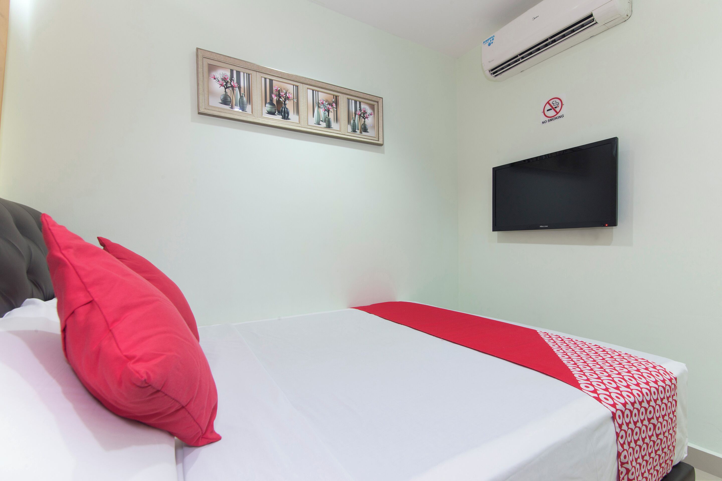 A hotel room with a bed, a TV, and a framed picture on the wall.