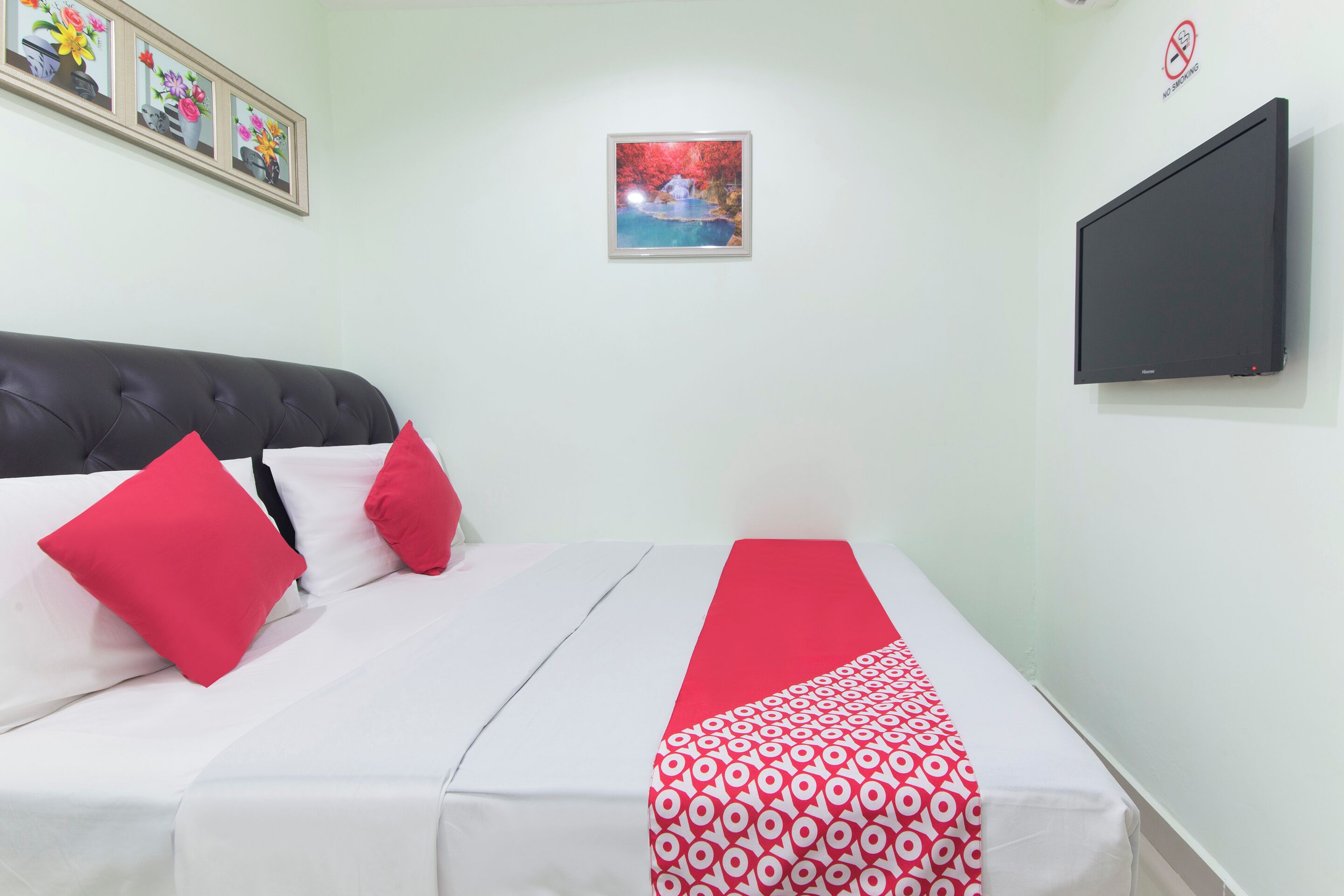 Habitación de hotel con una cama, almohadas rojas, un corredor de cama con estampado rojo y blanco, un cuadro en la pared y un televisor de pantalla plana.