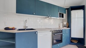 A modern kitchen with blue cabinets, a white countertop, a stainless steel sink, a built-in oven, and a white refrigerator. - "Niska" - 300m from the sea by Interhome (Sydals)