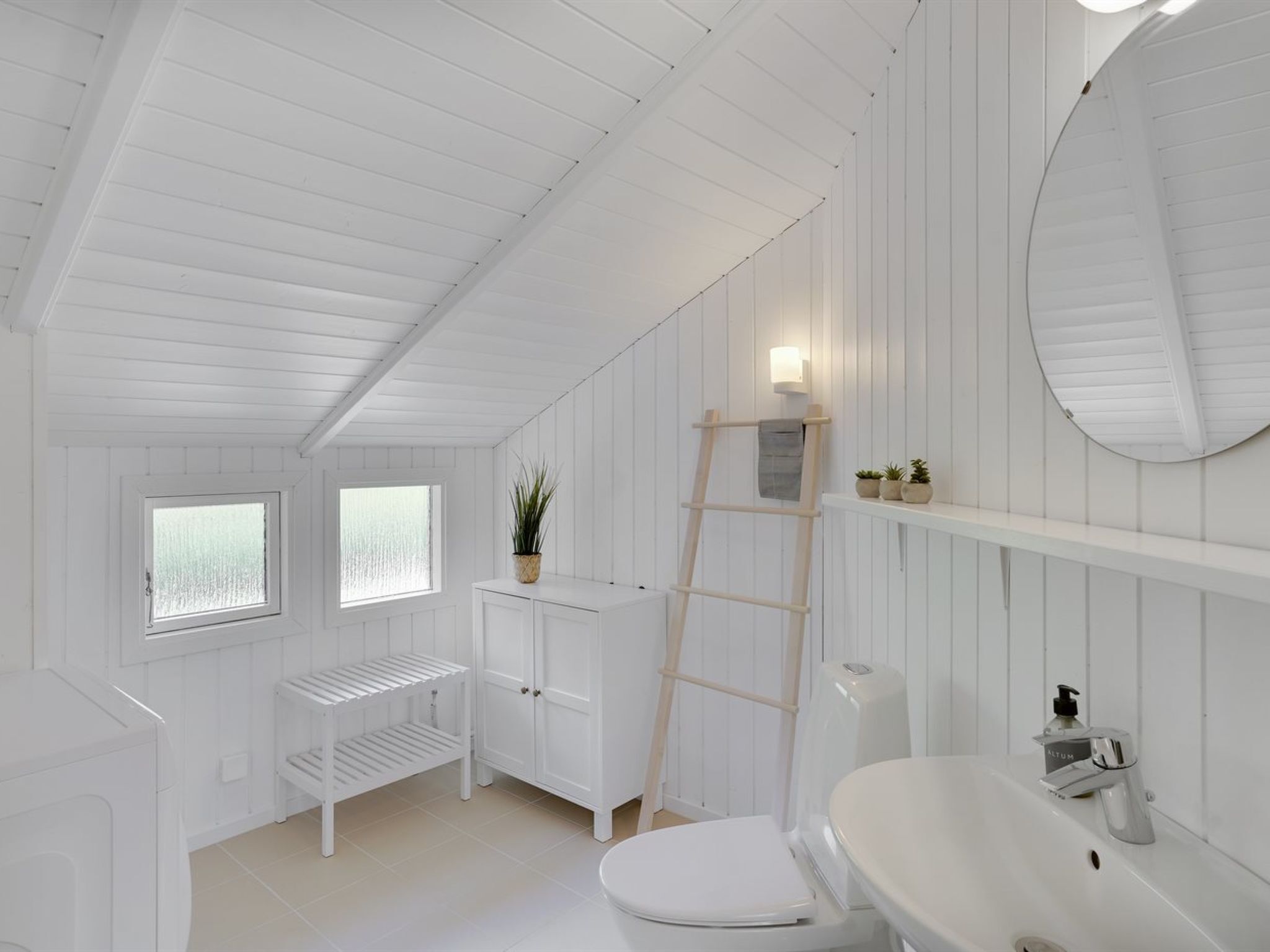 Une salle de bain en bois peinte en blanc, avec des toilettes, un lavabo et des étagères.