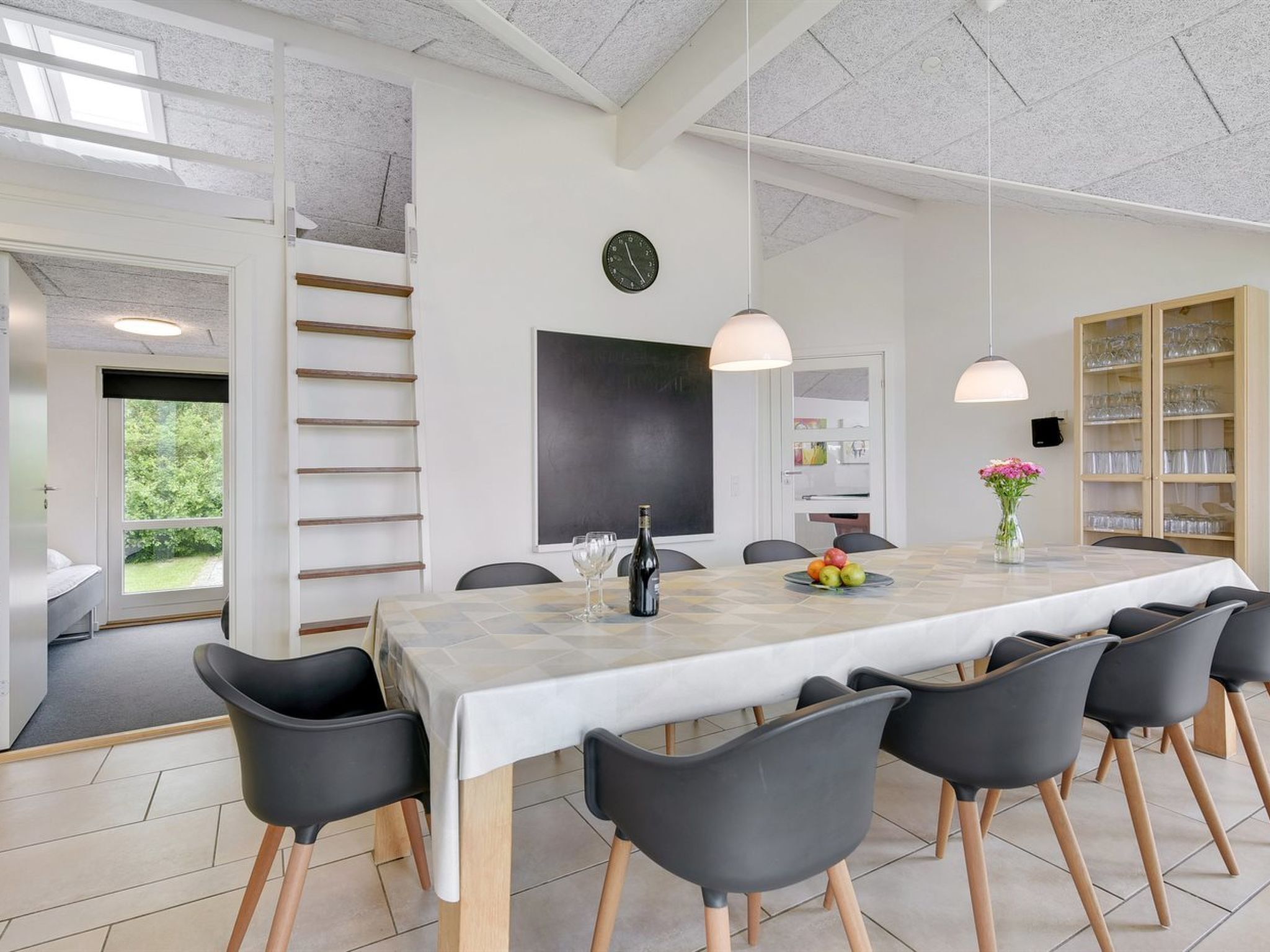 A dining area with a long table, black chairs, a wine bottle, and a fruit bowl.