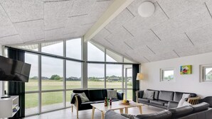 Ein geräumiges Wohnzimmer mit großen Fenstern, einem Flachbildfernseher, einer Couch, einem Couchtisch und einem Essbereich.